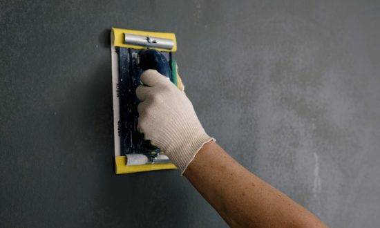 Ruka sa hoblom koja prelazi preko zida tamno sivih nijansi dok završava proces gletovanja